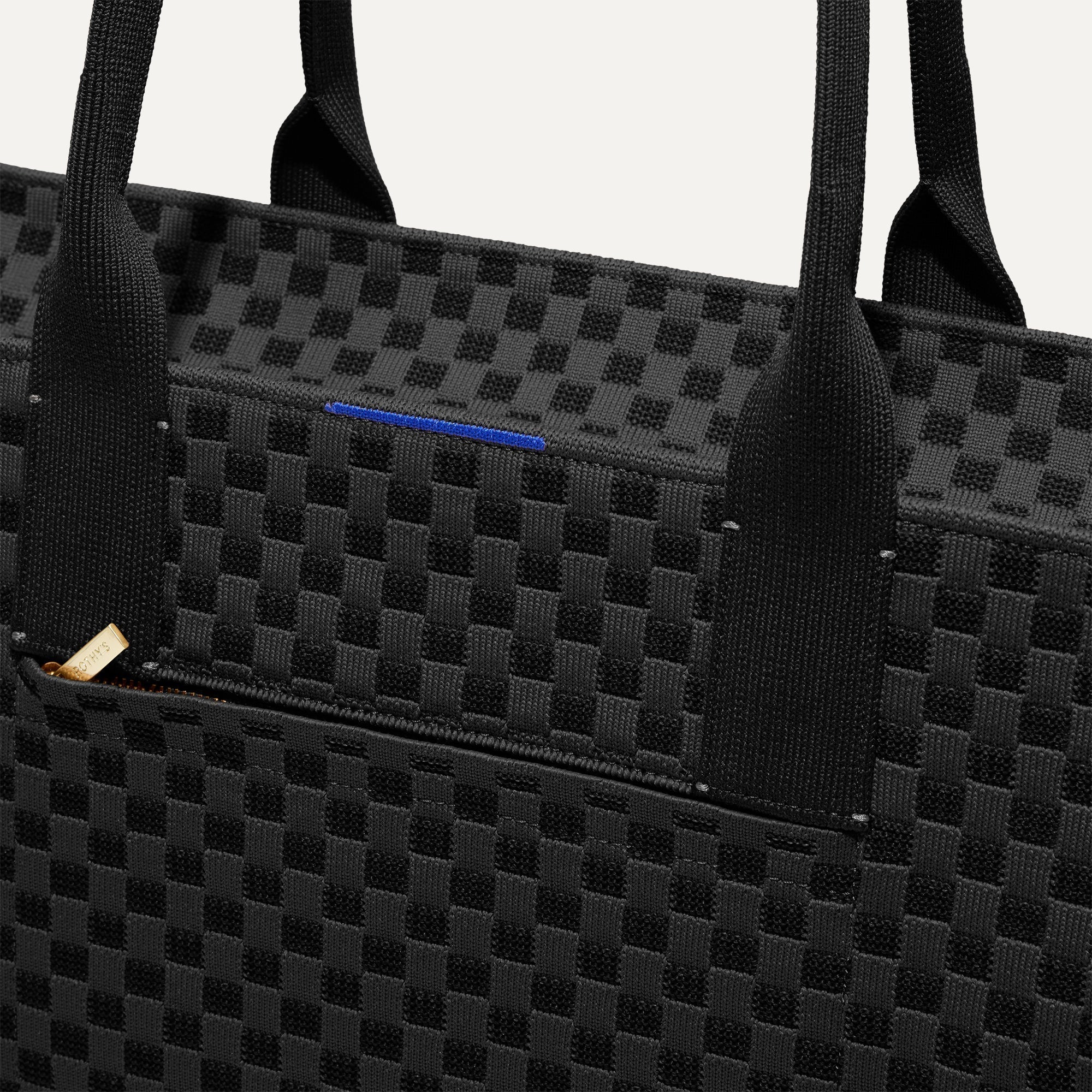 A closeup of The Classic Tote in Black Sand, focusing on the exterior zip pocket. 